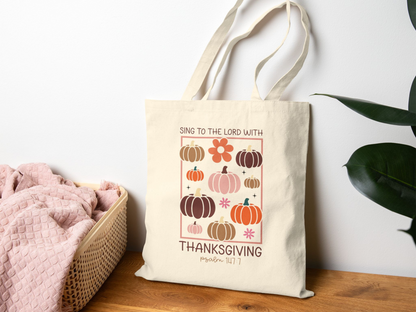 Tote bag on a rustic white background styled with a cozy sweater, pinecone, candle, and autumn leaves.