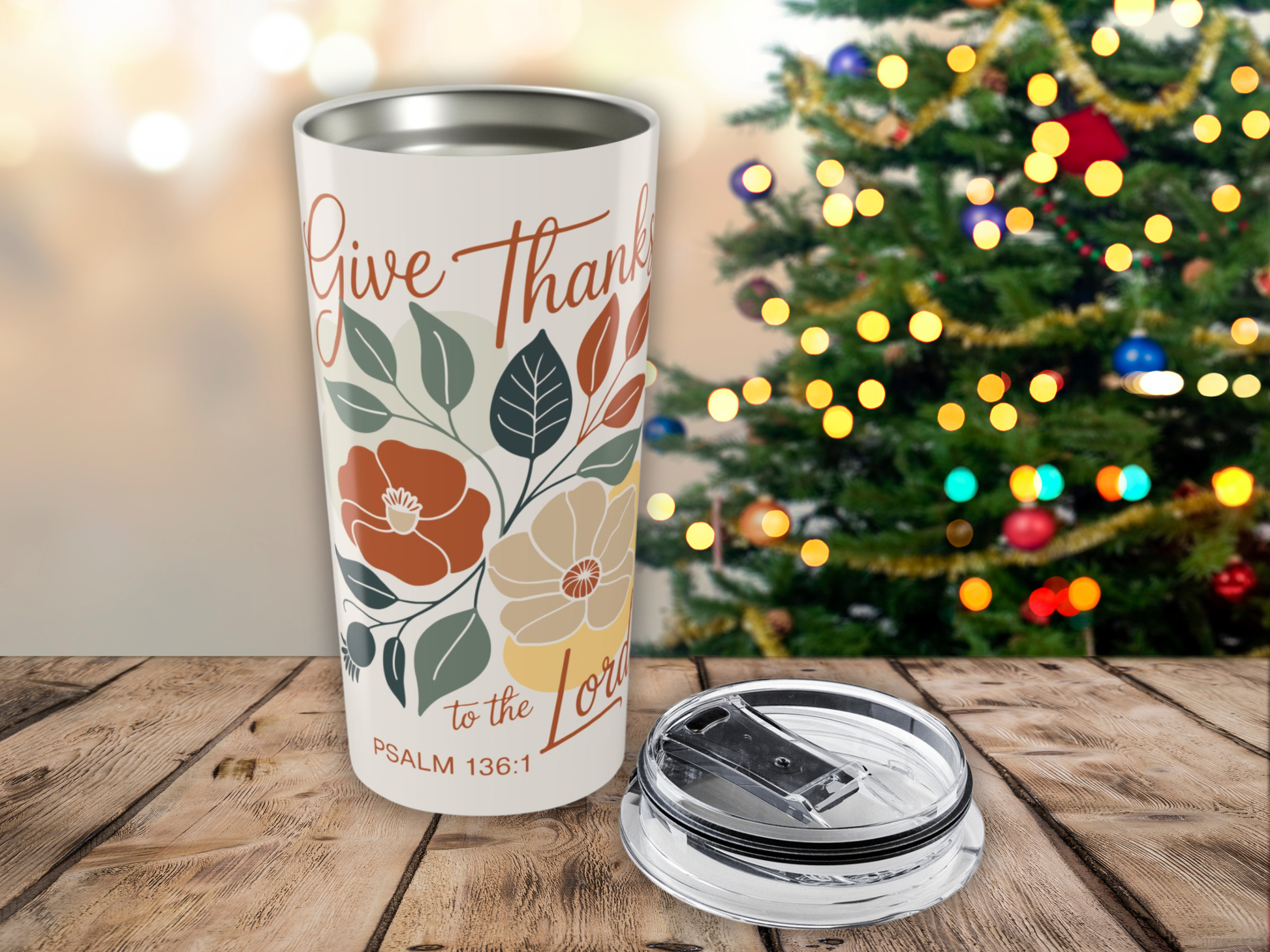 Tumbler with 'Give Thanks to the Lord' text and floral design in front of a decorated Christmas tree.