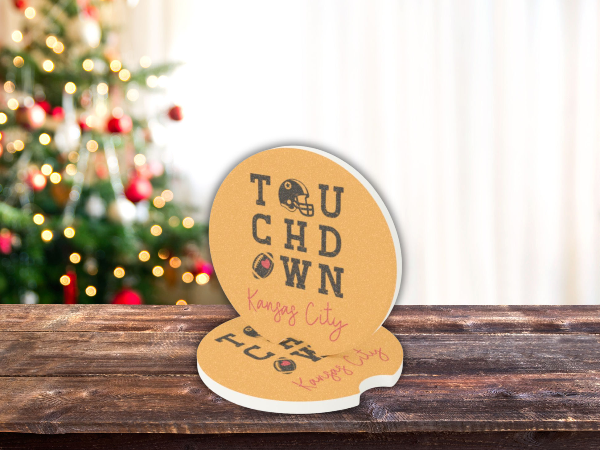 Decorative coasters with 'Touchdown Kansas City' text on a wooden surface with a Christmas tree in the background.