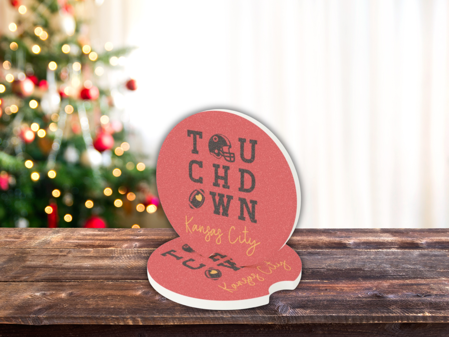 Decorative coasters with 'Touchdown Kansas City' text on a wooden surface with a blurred Christmas tree in the background.