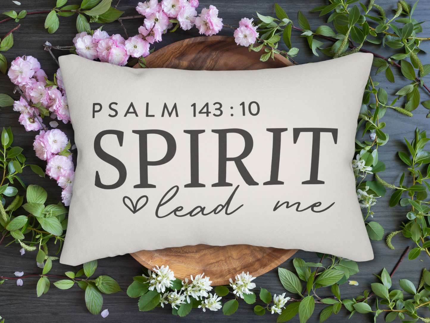 Decorative pillow with 'PSALM 143:10 SPIRIT lead me' text, surrounded by flowers and leaves on a dark surface.