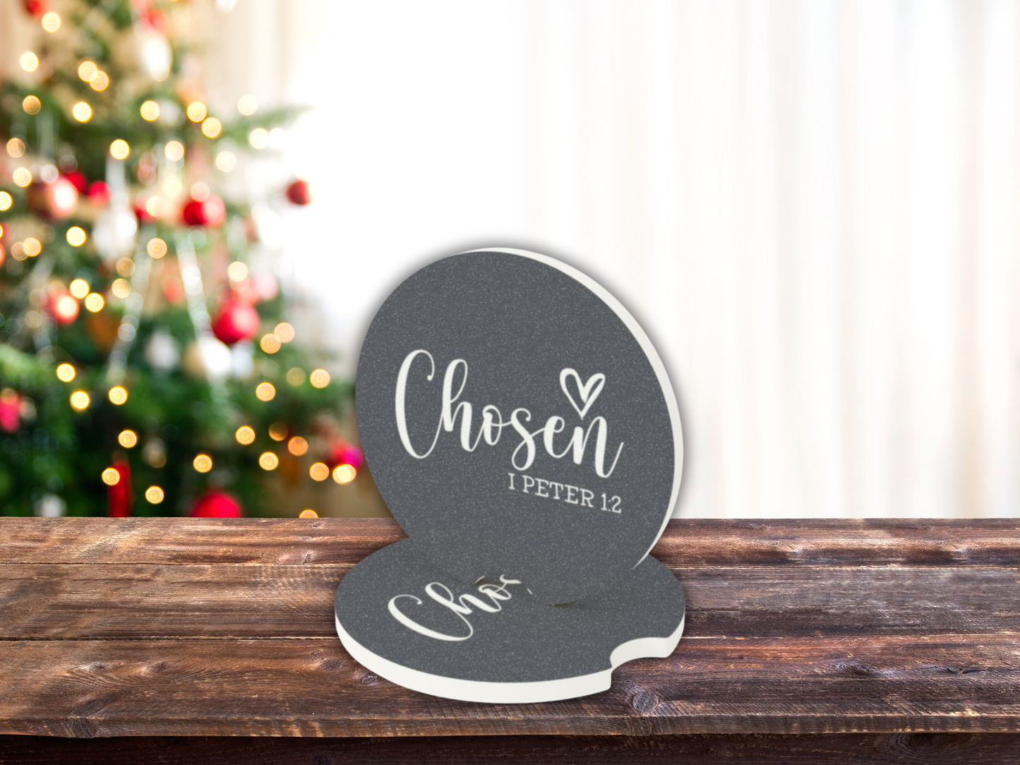 Decorative car coasters with 'Chosen 1 Peter 1:2' text on a wooden surface with a blurred Christmas tree in the background.