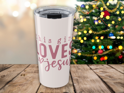 Pink tumbler with 'this girl loves Jesus' text in pink, placed on a wooden surface with a Christmas tree in the background.