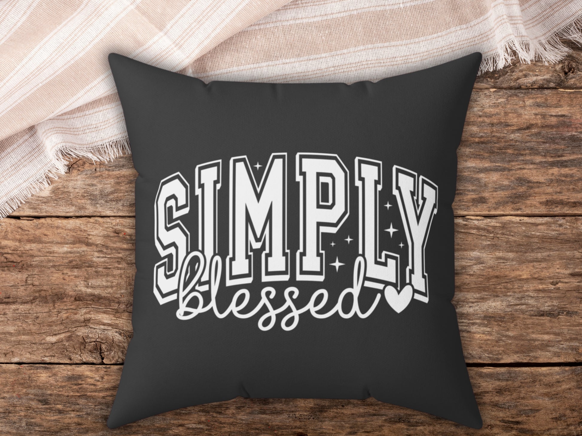 Black pillow with 'Simply blessed' text on a wooden surface