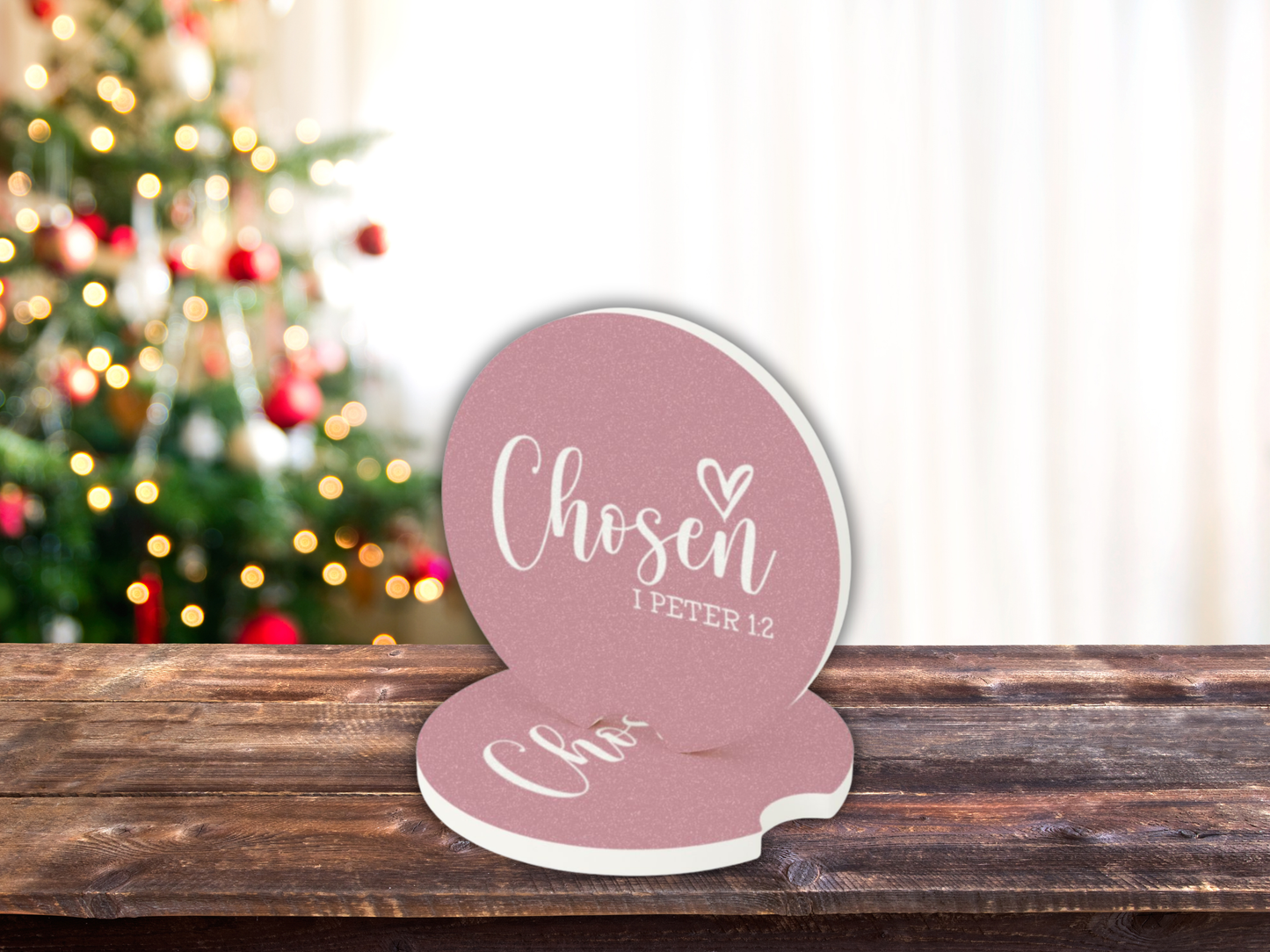 Decorative car coasters with 'Chosen' text on a wooden surface with a Christmas tree in the background