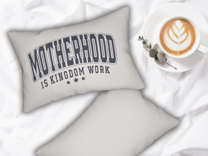 Pair of pillows on a white bedspread, one displaying the “Motherhood is Kingdom Work” design beside a latte and greenery.
