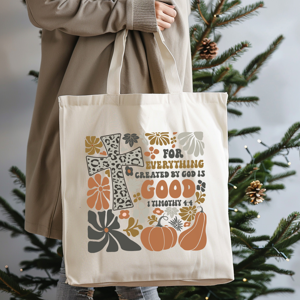 Tote bag with decorative design and text held by a person in front of a Christmas tree.