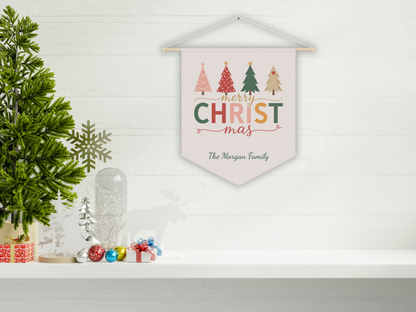 Decorative wall hanging with 'Merry Christmas' text and trees, placed on a shelf with festive decor.