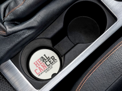 Car cup holder with a circular coaster labeled 'HEAL CANCER' on a black leather interior.