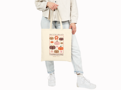 Person holding tote bag at their side while wearing casual neutral clothing and sneakers.