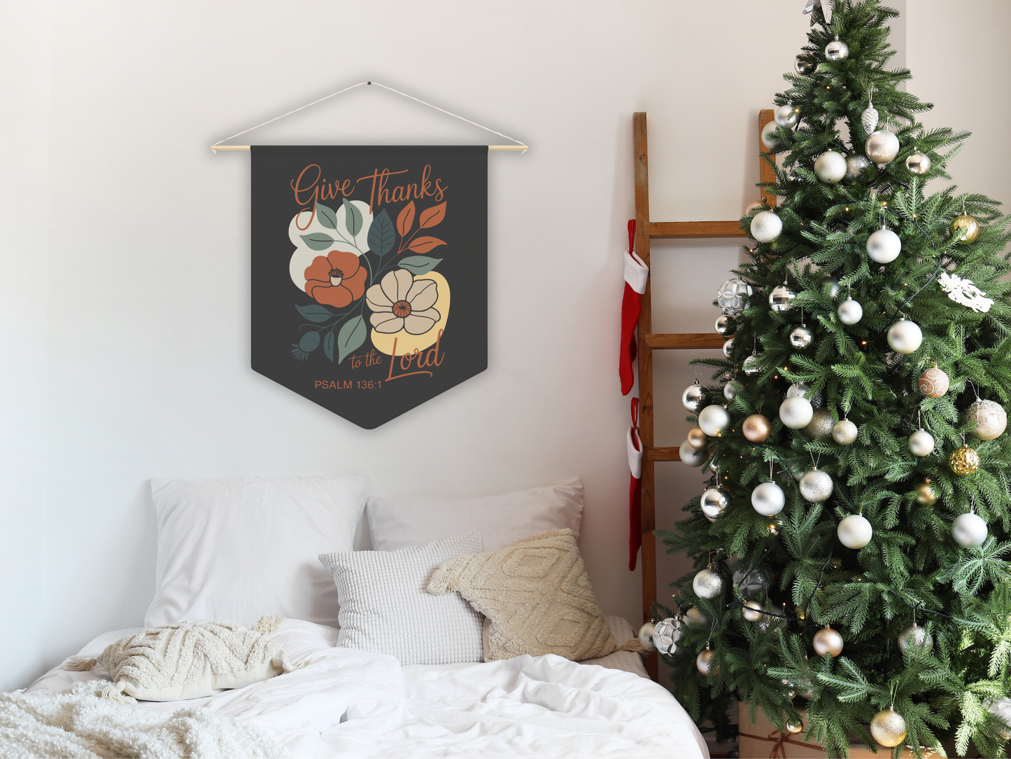 Decorative wall hanging with floral design and text above a bed with a Christmas tree in the corner.