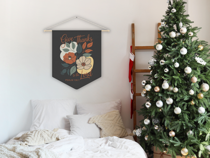 Decorative wall hanging with floral design and text above a bed with a Christmas tree in the corner.