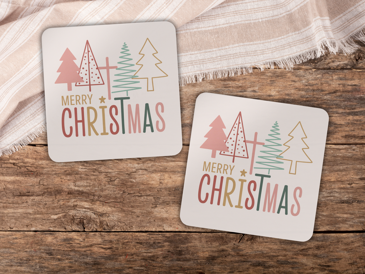 Two Christmas-themed coasters with trees and 'Merry Christmas' text on a wooden surface.
