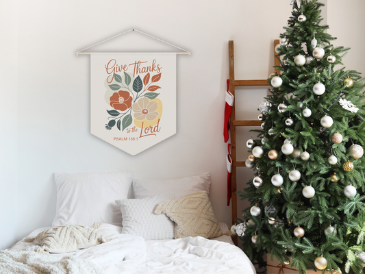 Decorative wall hanging with floral design and text above a bed with a Christmas tree on the side.