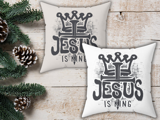Two pillows with 'Jesus is King' design on a wooden surface with Christmas decorations.