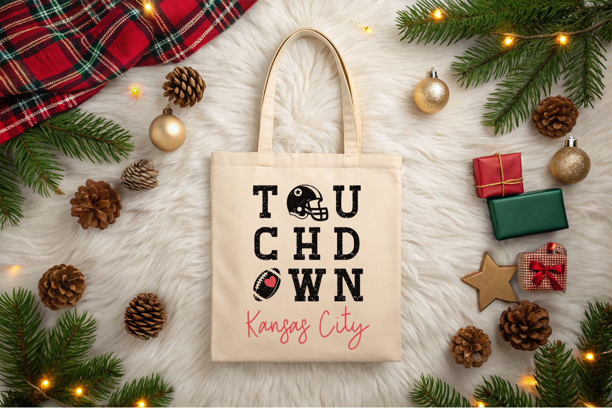 Tote bag with 'Touchdown Kansas City' text surrounded by Christmas decorations on a light surface.
