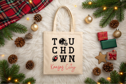Tote bag with 'Touchdown Kansas City' text surrounded by Christmas decorations on a light surface.