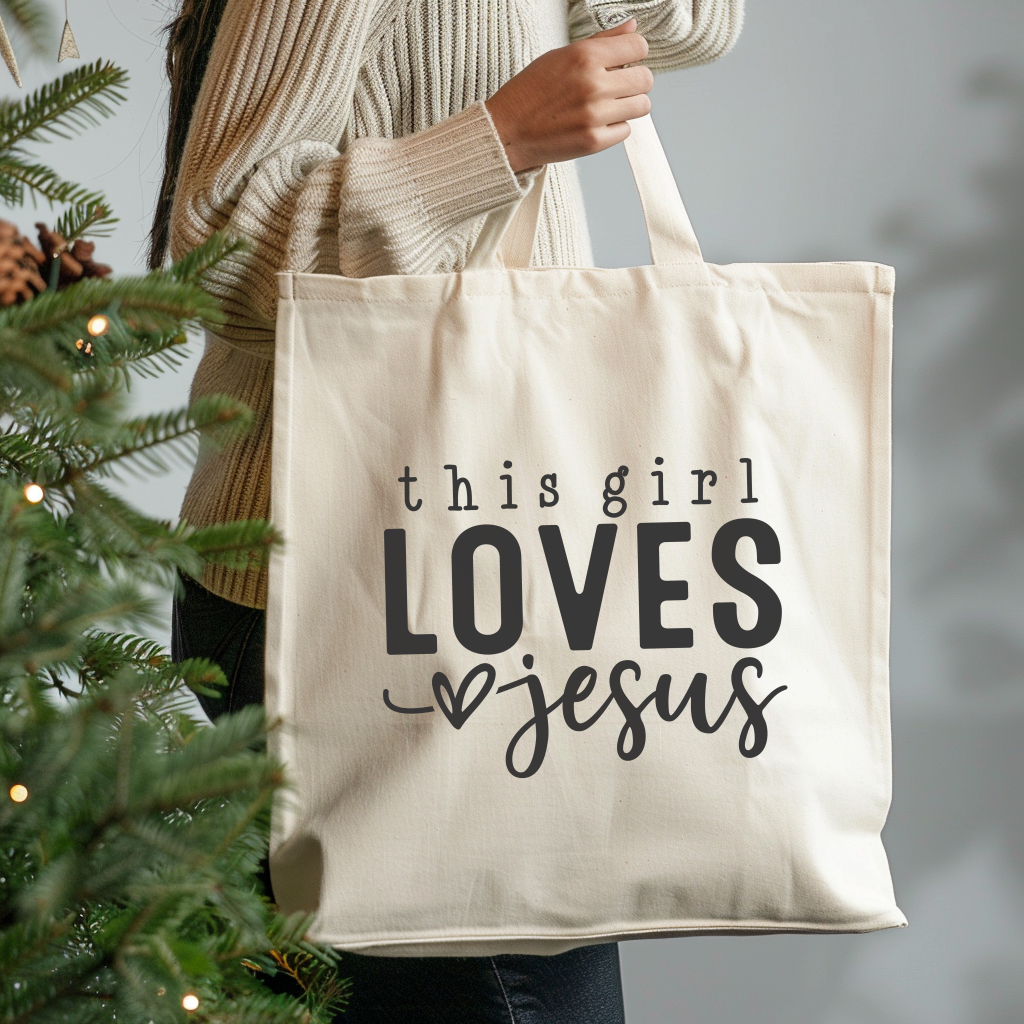 Tote bag with 'this girl LOVES Jesus' text held by a person next to a Christmas tree.