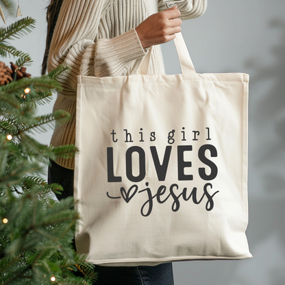 Tote bag with 'this girl LOVES Jesus' text held by a person next to a Christmas tree.