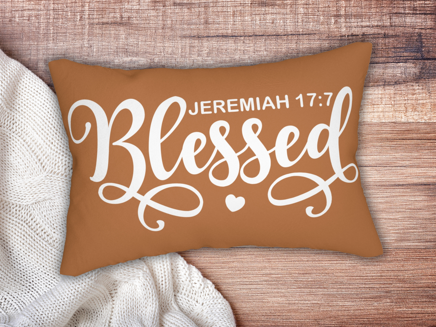 Brown scripture pillow on a wooden background, paired with a chunky white knit blanket.