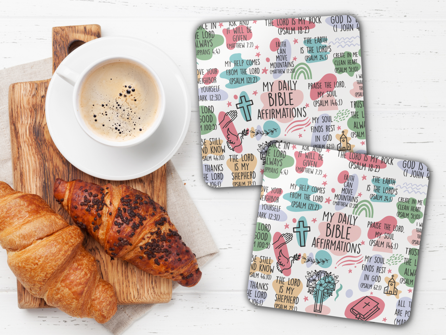 Two Bible affirmation coasters styled with coffee, croissants, and wooden serving board on a bright white table.