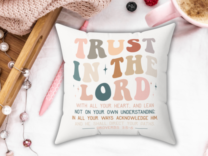 White throw pillow with colorful “Trust in the Lord” Proverbs 3:5-6 scripture, styled with pink mug, pen, berries, and wooden tray on white bedding.
