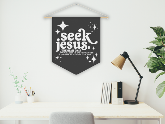Decorative banner with 'seek Jesus' text hanging above a desk in a home office setting.
