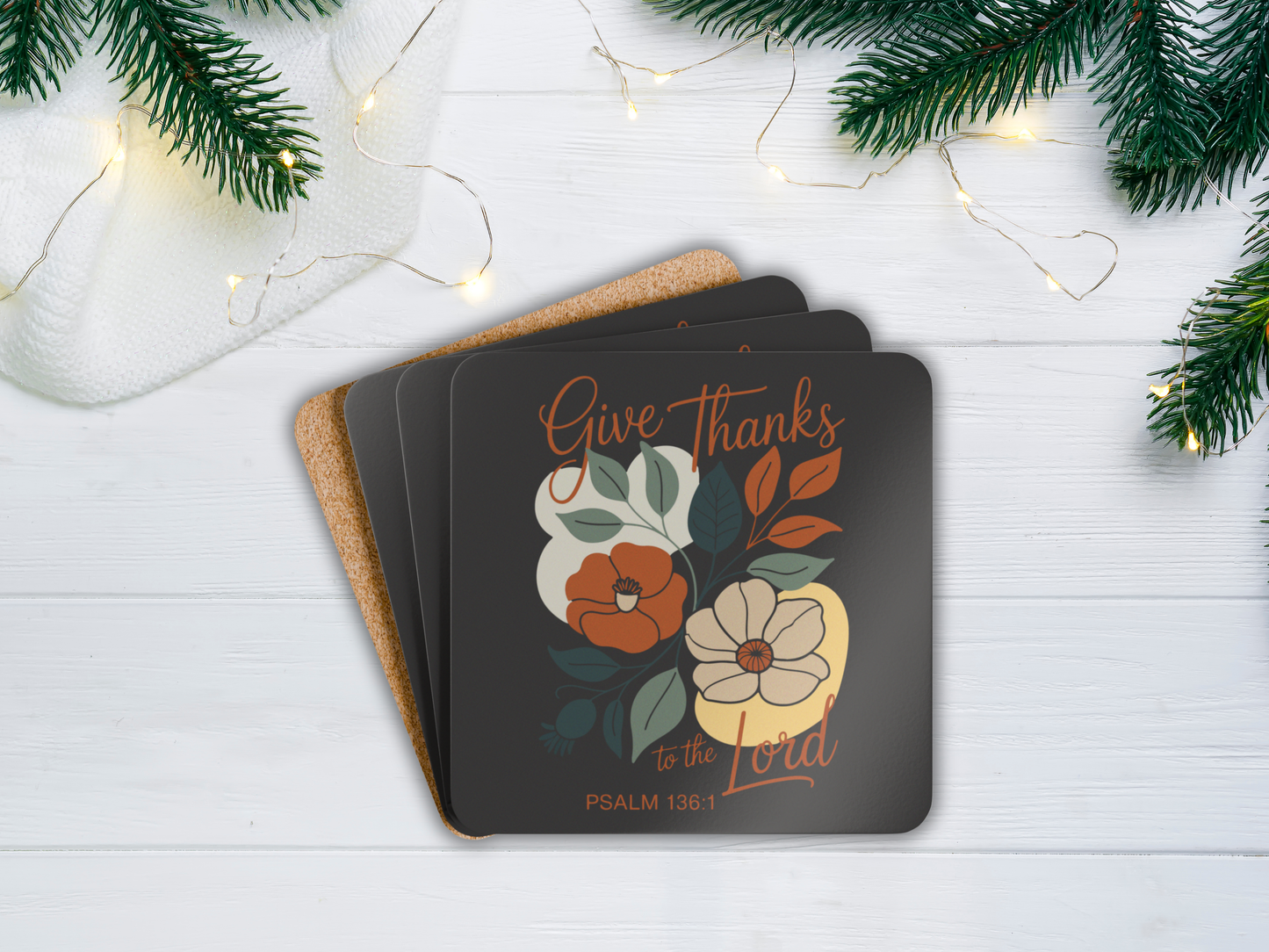 Coasters with floral design and 'Give Thanks' text on a white surface with Christmas decorations.