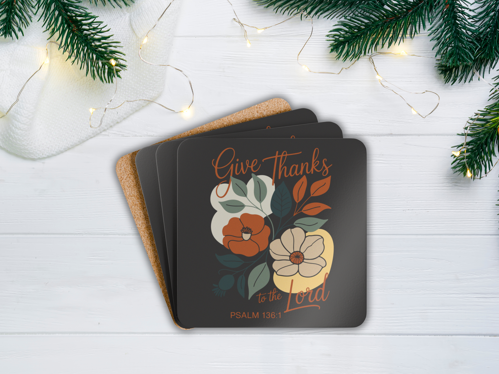 Coasters with floral design and 'Give Thanks' text on a white surface with Christmas decorations.