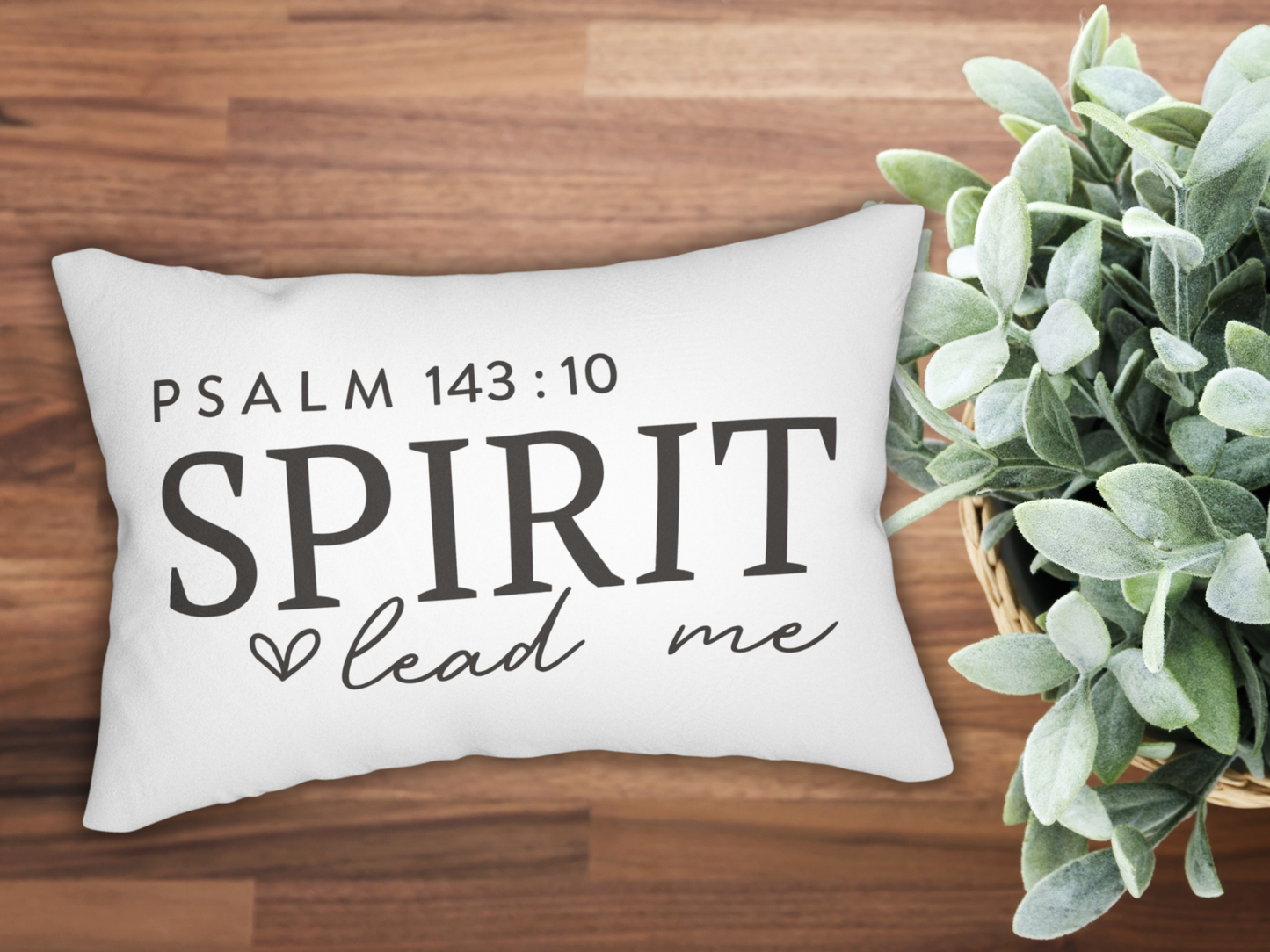 Decorative pillow with 'Psalm 143:10 Spirit lead me' text on a wooden surface with a plant.