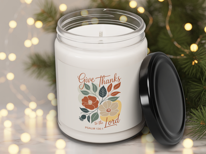 White candle jar with 'Give Thanks to the Lord' text and floral design, surrounded by festive lights and greenery.