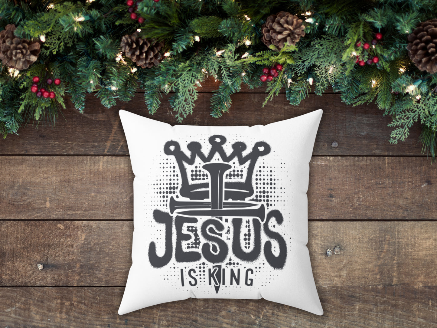 White pillow with 'Jesus is King' text on a wooden surface with Christmas decorations.