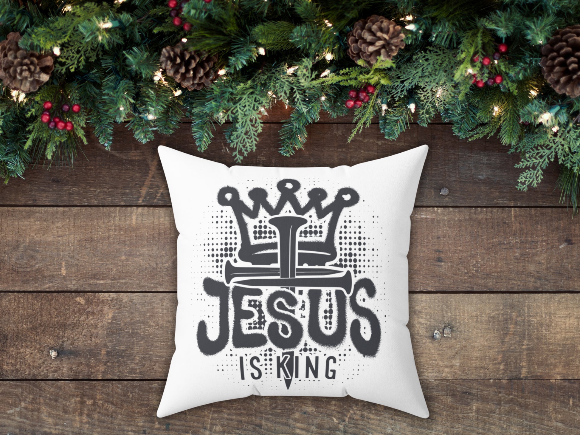White pillow with 'Jesus is King' text on a wooden surface with Christmas decorations.