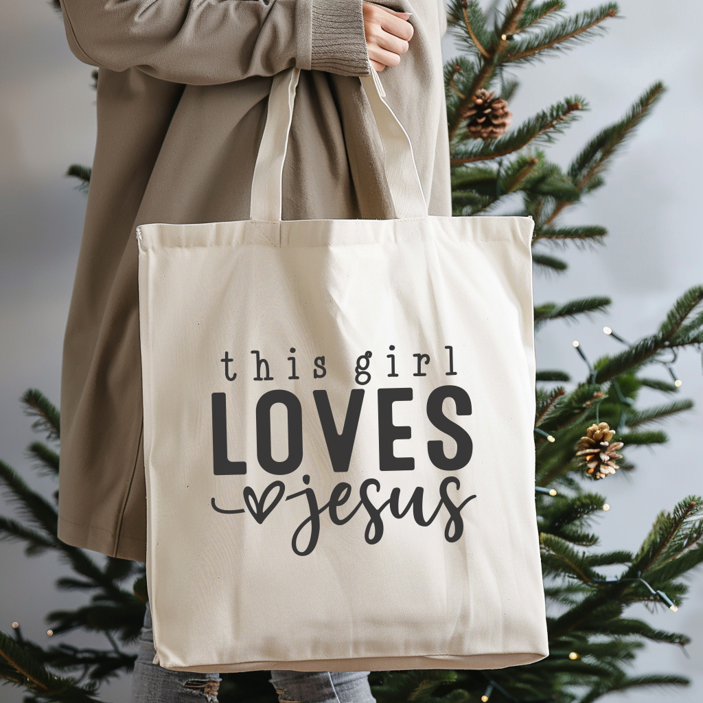 Tote bag with 'this girl LOVES jesus' text held by a person in front of a Christmas tree.