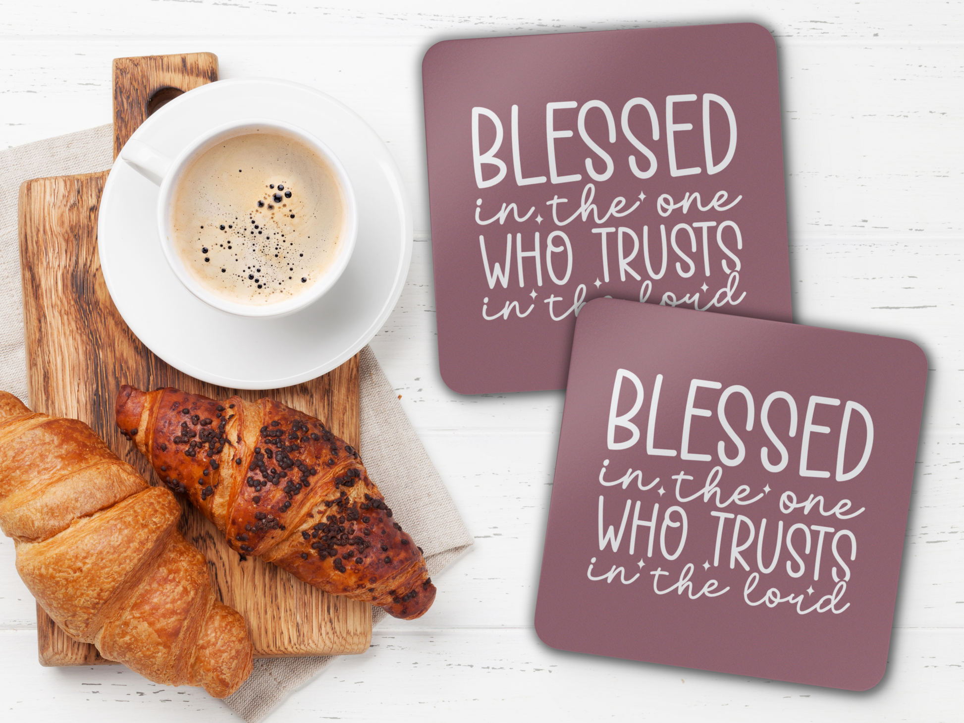 Two coasters beside coffee and croissants on a wooden board over a white tabletop.