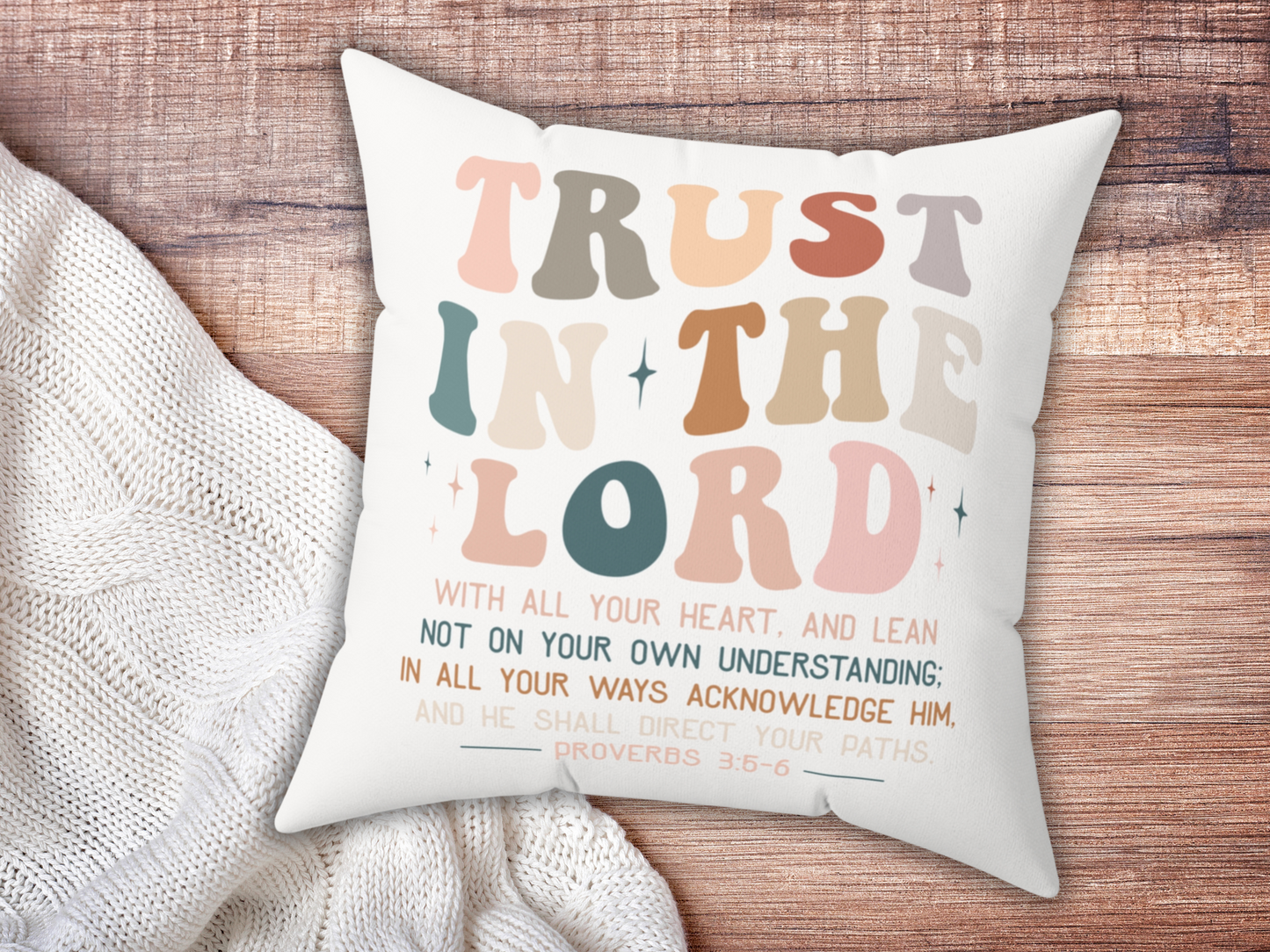 Christian scripture pillow with “Trust in the Lord” text, placed on wooden surface beside cozy cream knit blanket.