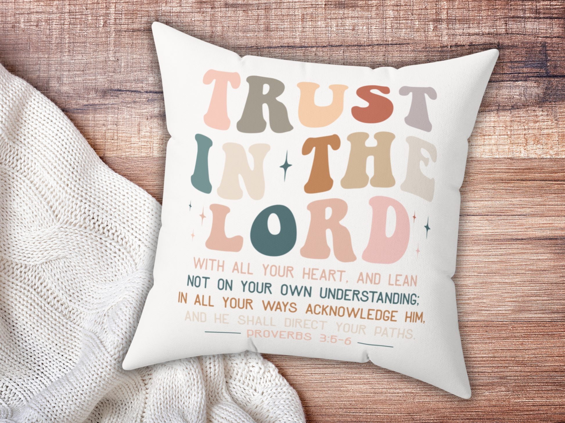 Christian scripture pillow with “Trust in the Lord” text, placed on wooden surface beside cozy cream knit blanket.