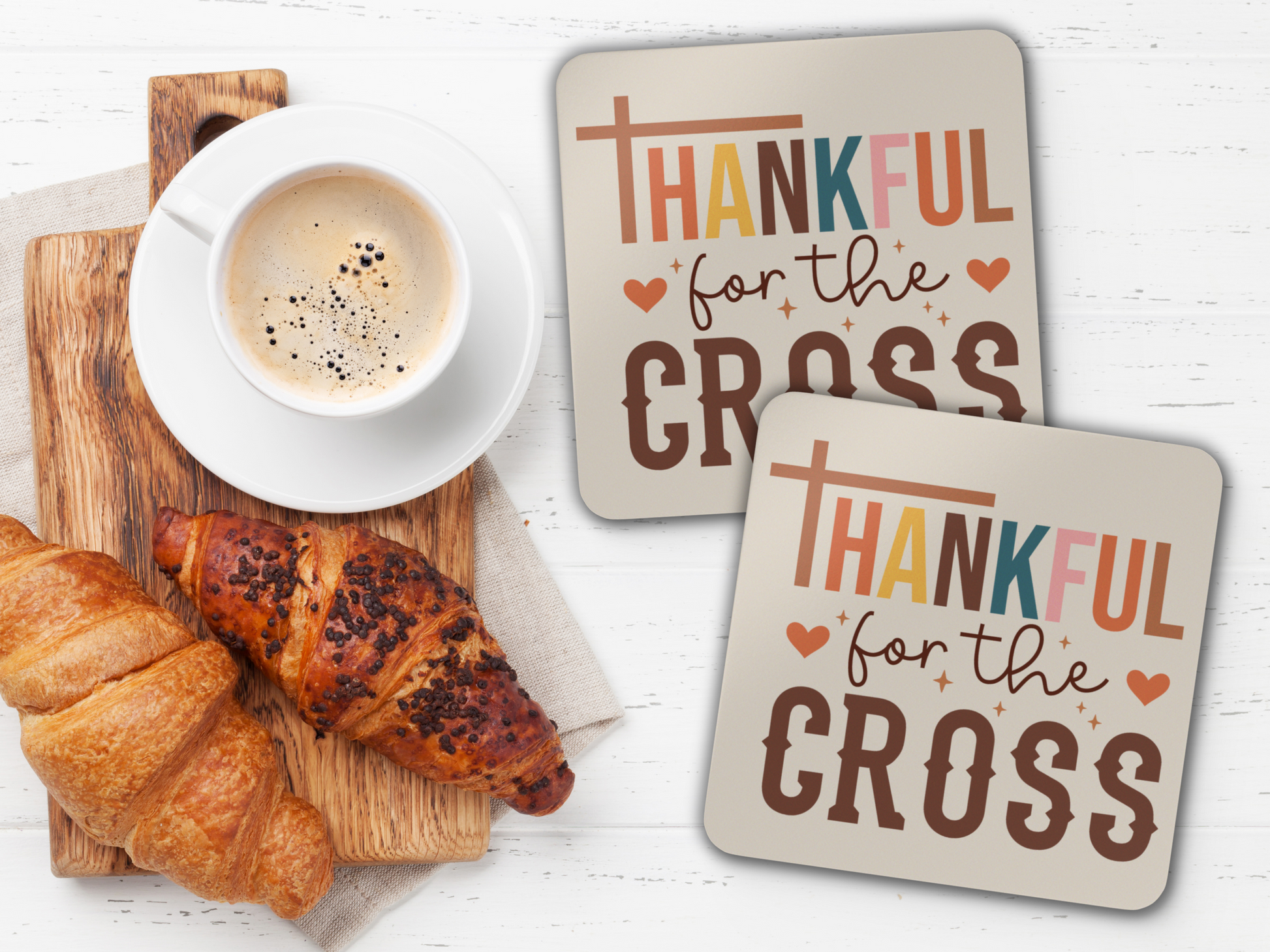 Pair of scripture coasters with coffee and croissants on rustic wooden serving board over white table.