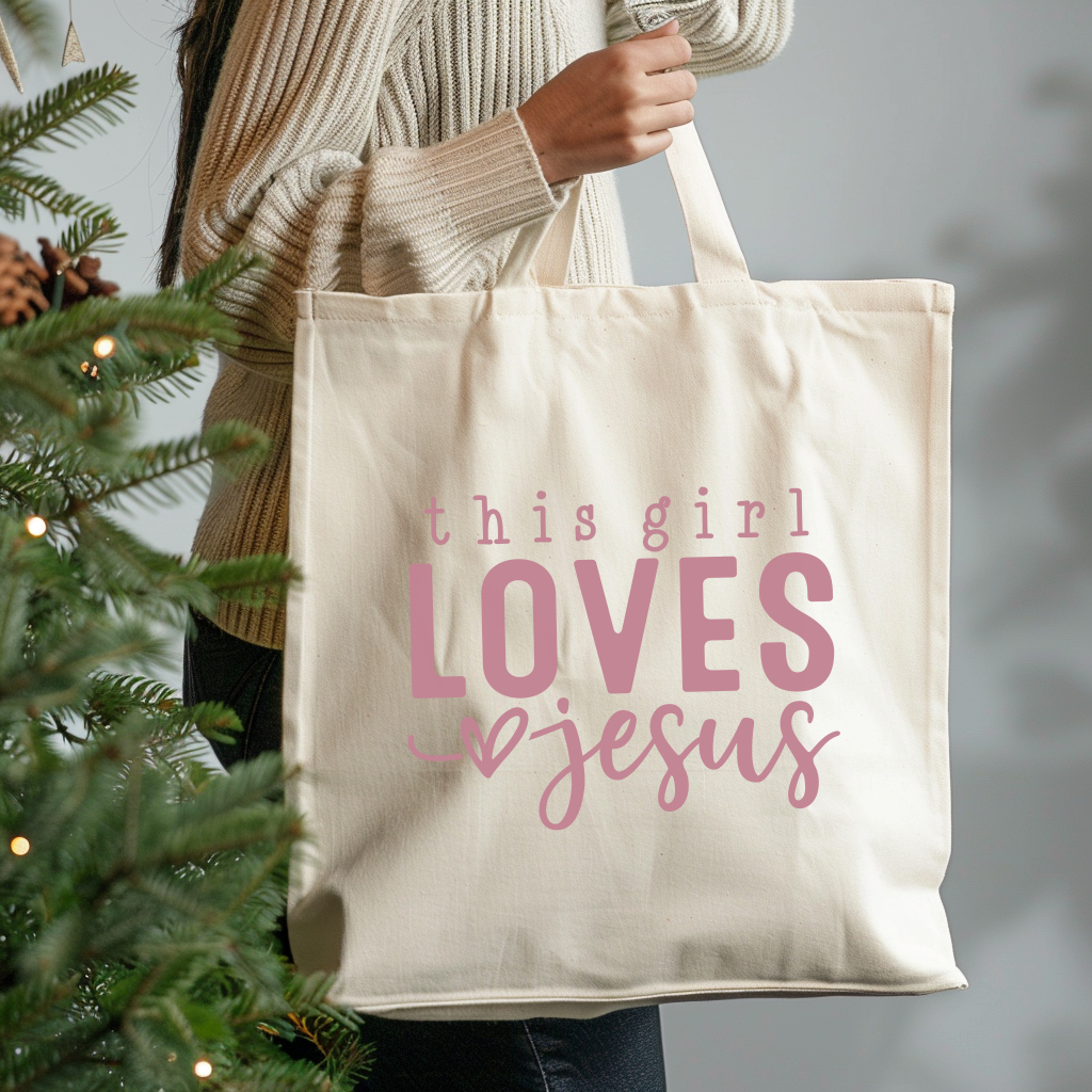 Tote bag with 'this girl LOVES Jesus' text held by a person next to a Christmas tree.
