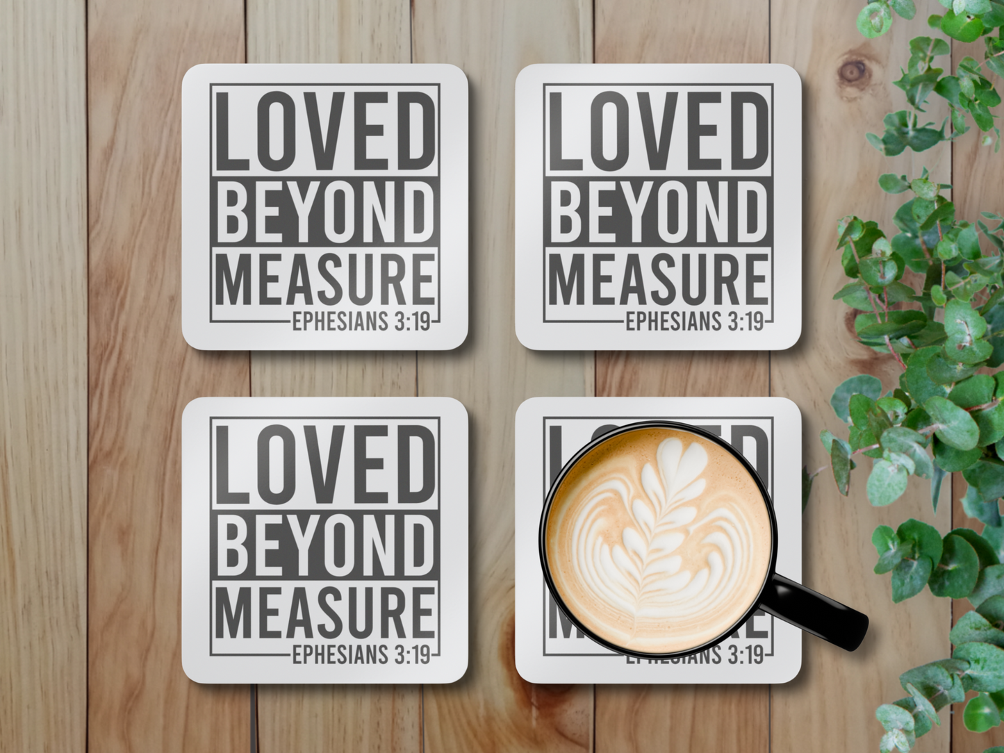 Four coasters on a light wooden surface, one holding a latte in a black cup, styled with greenery.