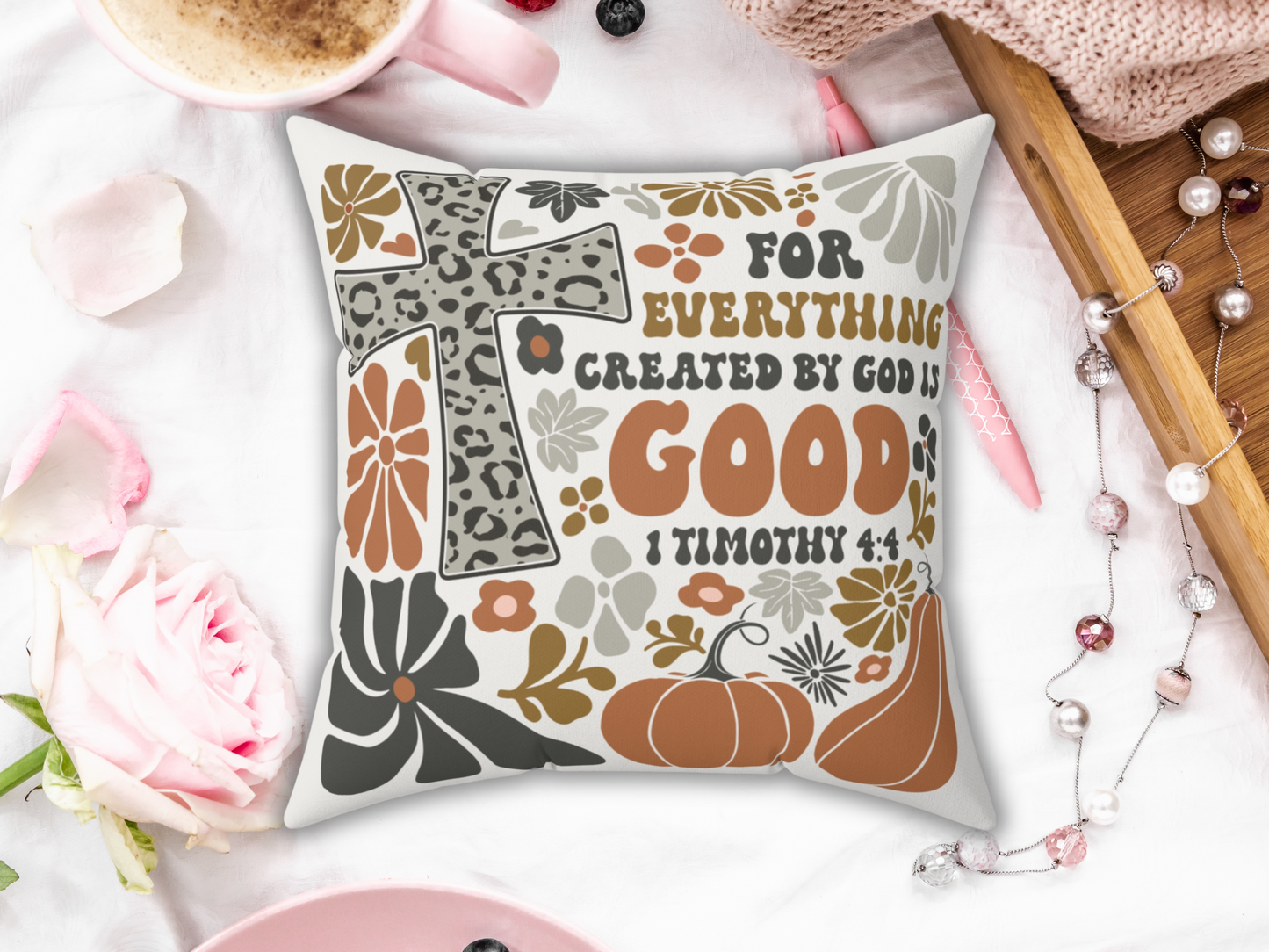 Scripture pillow reading “For everything created by God is good,” placed on white bedding with pink rose, coffee, pen, and wooden tray.