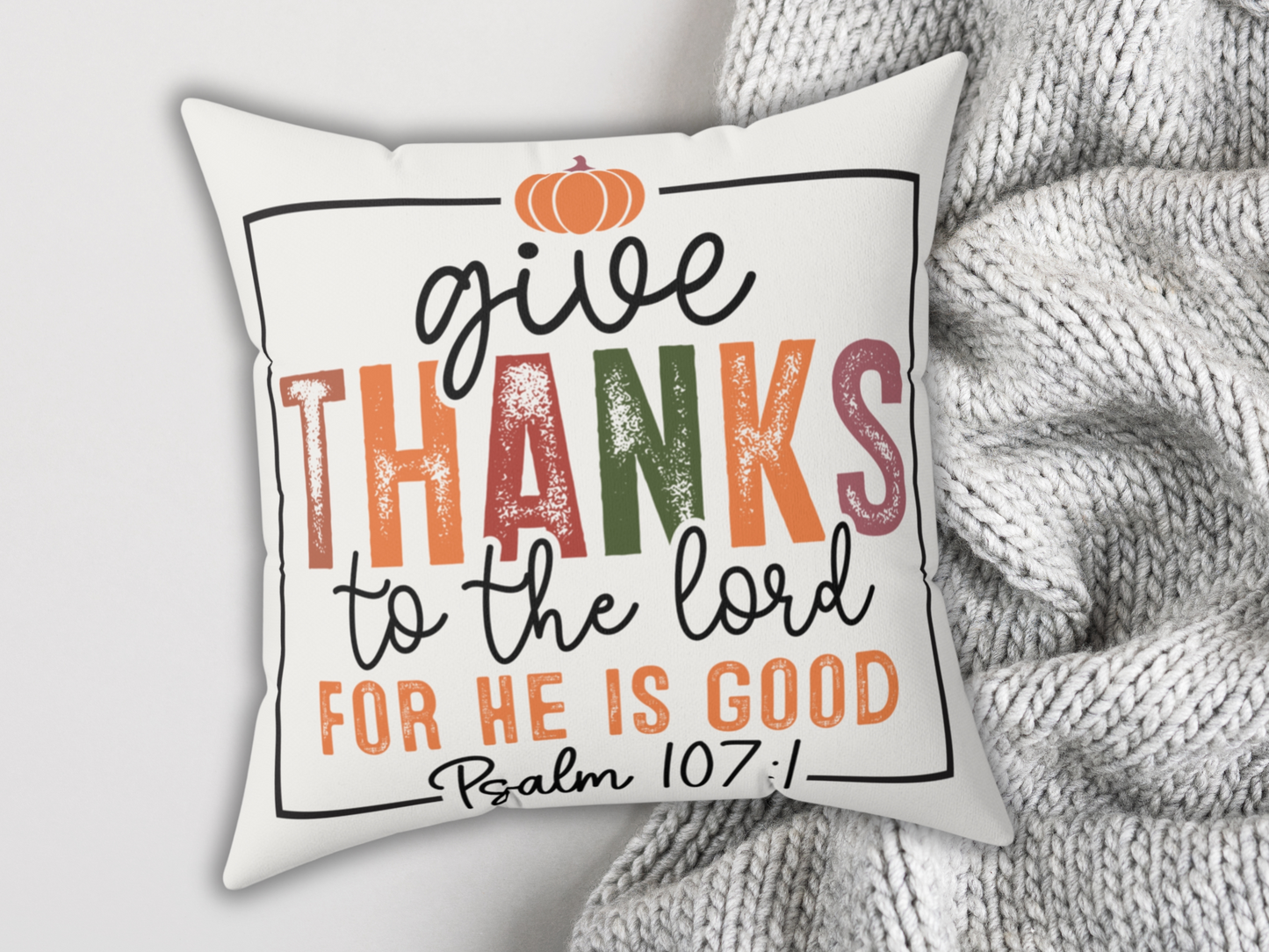 White pillow with Psalm 107:1 design styled with chunky gray knit blanket for a cozy autumn look.