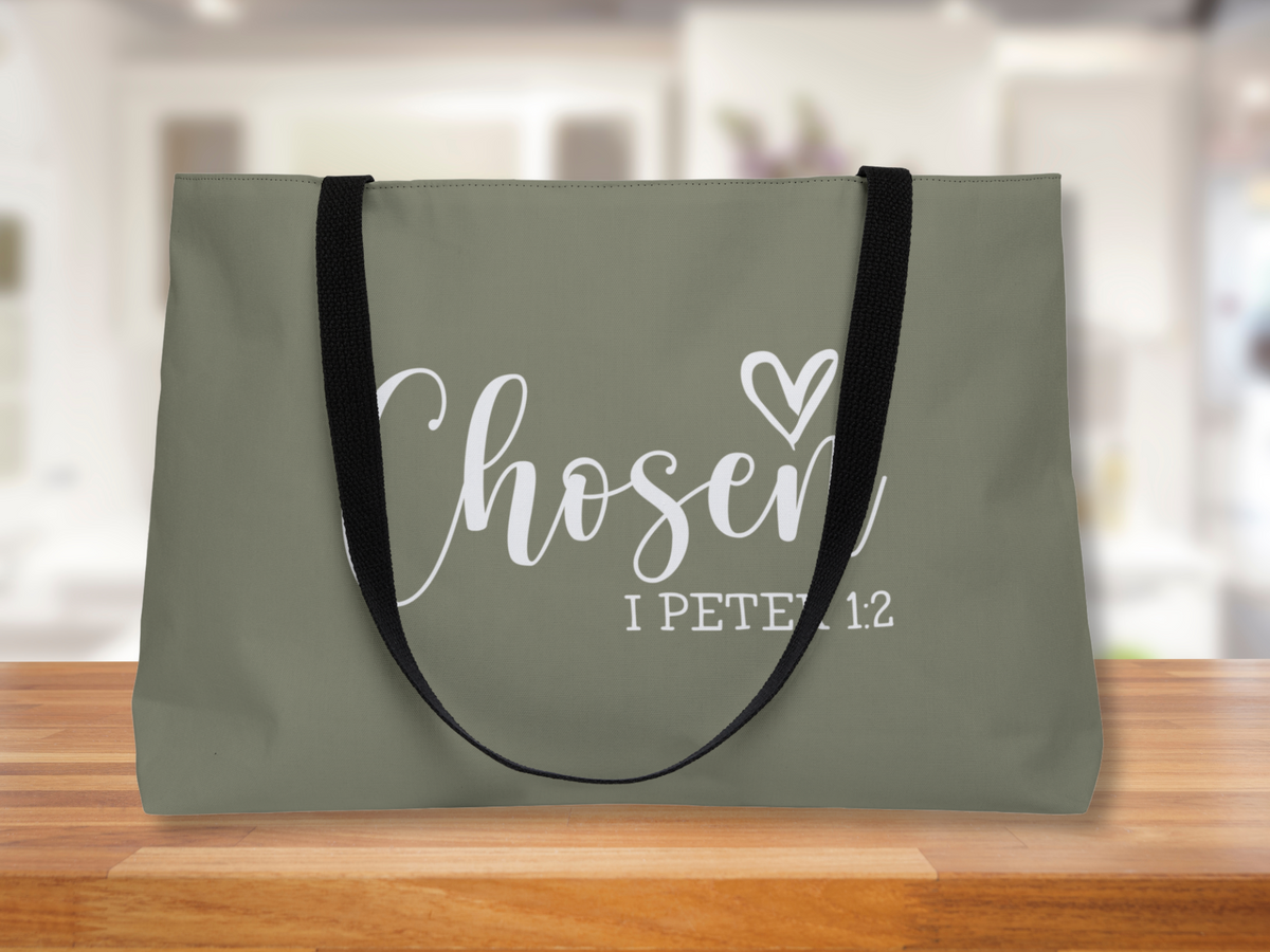 “Chosen – I Peter 1:2” olive green tote with black straps displayed on a wooden surface against a soft blurred background.