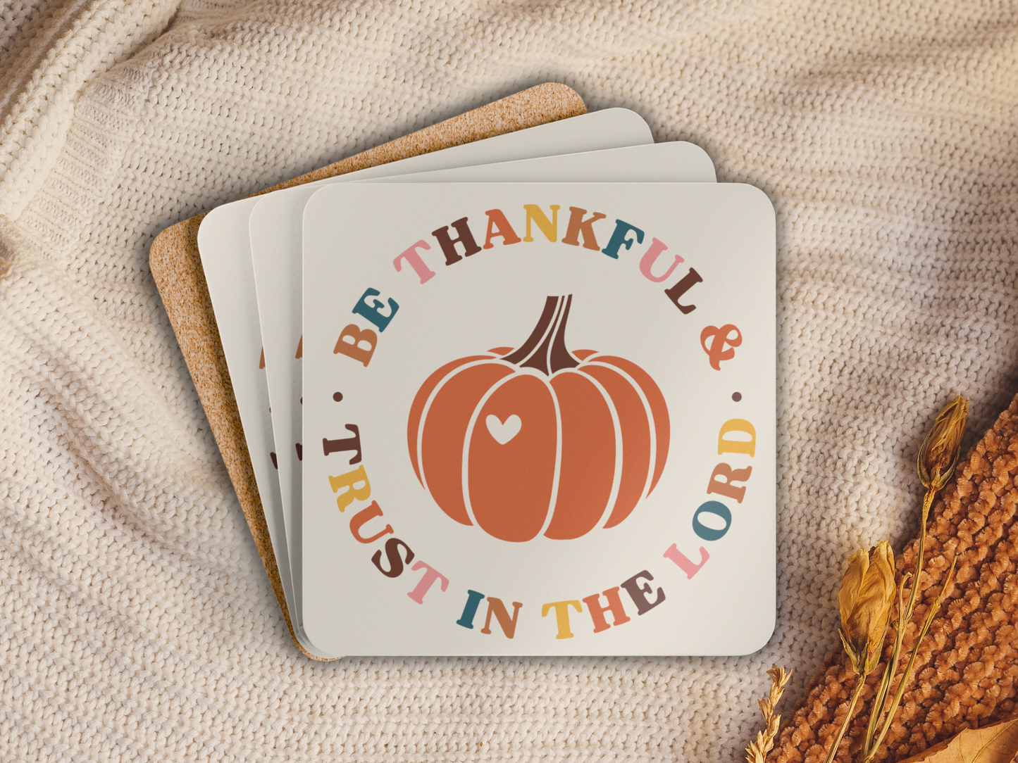 Stack of pumpkin-themed scripture coasters with cork backing styled on a cozy knit blanket with autumn accents.