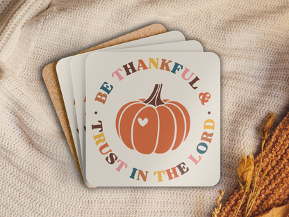 Stack of pumpkin-themed scripture coasters with cork backing styled on a cozy knit blanket with autumn accents.