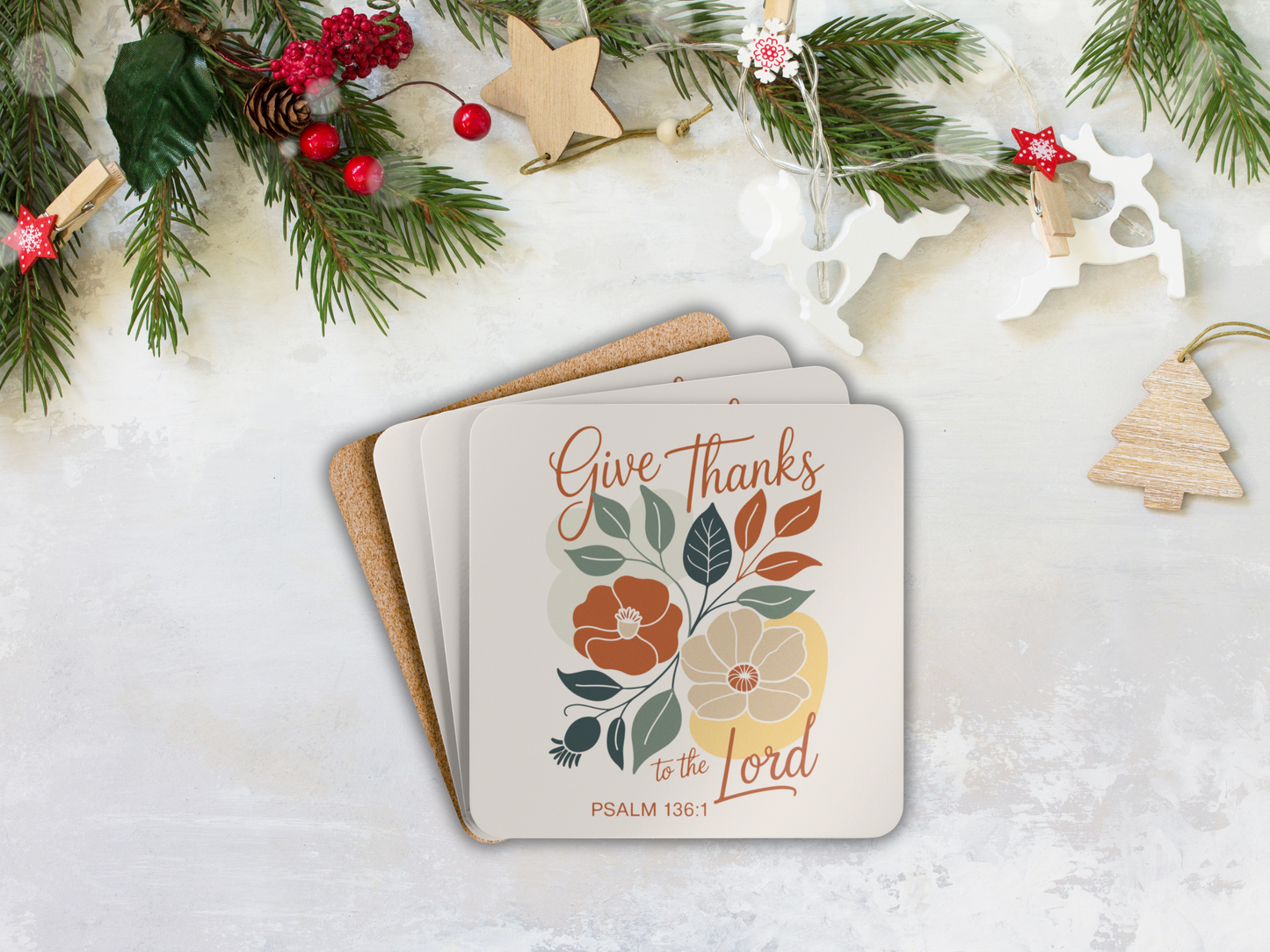 Stack of coasters with floral design and text 'Give Thanks to the Lord' on a snowy background with Christmas decorations.