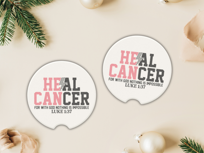 Two circular 'Heal Cancer' car coasters on a light surface with Christmas decorations.