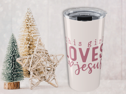 Pink tumbler with 'this girl loves Jesus' text next to Christmas trees on a light background
