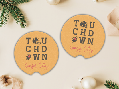 Two round coasters with 'Touchdown Kansas City' text on a beige surface with Christmas decorations.