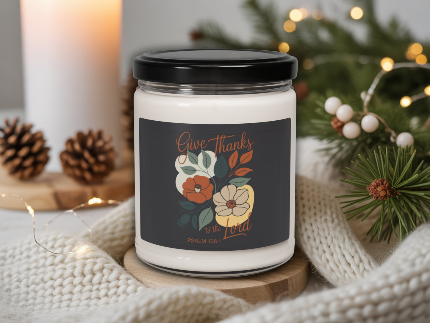 Candle jar with 'Give Thanks' label on a decorative setting with lights and pine cones.